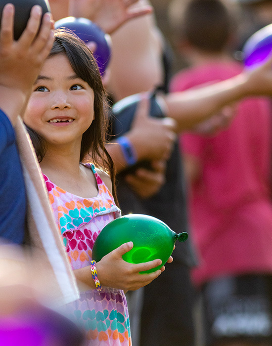 Water balloon toss, girl in rainbow dress holding green balloon